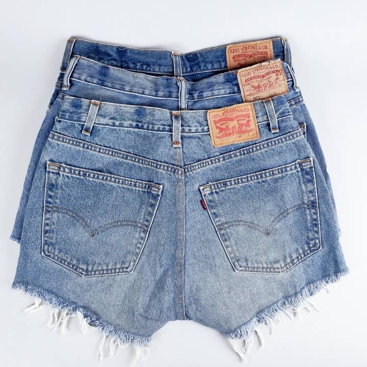 Three pairs of Levi's Vintage Denim Cutoff Shorts in light blue with frayed hems, laid flat to display back pockets and leather patches—a stylish, sustainable pick from Levis.