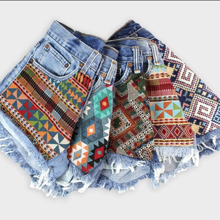 Five pairs of Levi’s High-Rise Vintage Denim Cutoff Shorts feature frayed hems and unique, colorful woven recycled tapestry patches on the front.