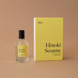 A bottle of dilo's Hinoki Sesame Eau De Parfum stands beside its yellow box on a plain brown background, showcasing the fragrance by dilo.