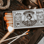 An open box of Mollyjogger Hounds Safety Matches shows several matches inside, with one lit match in front. The box design evokes classic cigar matches and is branded "Hounds Safety Matches | Mollyjogger.