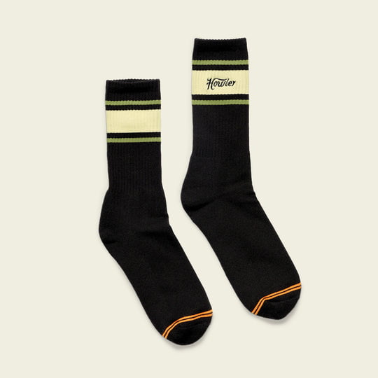 The Howler Brothers Script Socks feature a black crew design with green and yellow stripes, orange toe accents, and "Howler" text on the side for a vintage-inspired look.