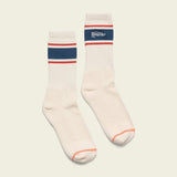 The Howler Brothers Script Socks are white athletic crew socks with blue and red stripes, "Howler" on the cuff, orange toe accents, and soft combed cotton for lasting comfort.