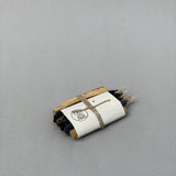 The Sampler Incense Bundle | Incausa features dark sticks, palo santo, and wood pieces wrapped in white paper and twine on a plain gray surface.