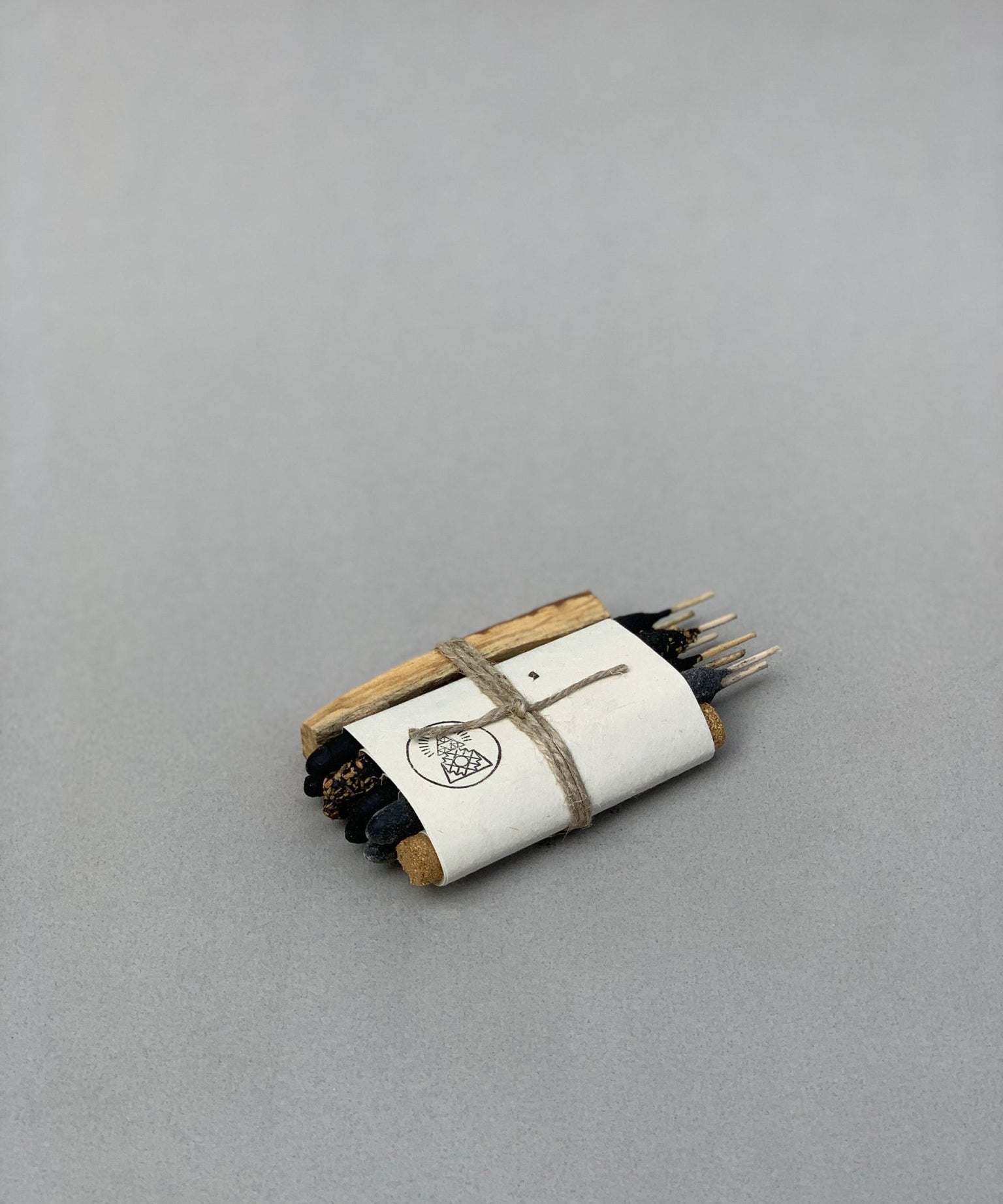 The Sampler Incense Bundle | Incausa features dark sticks, palo santo, and wood pieces wrapped in white paper and twine on a plain gray surface.