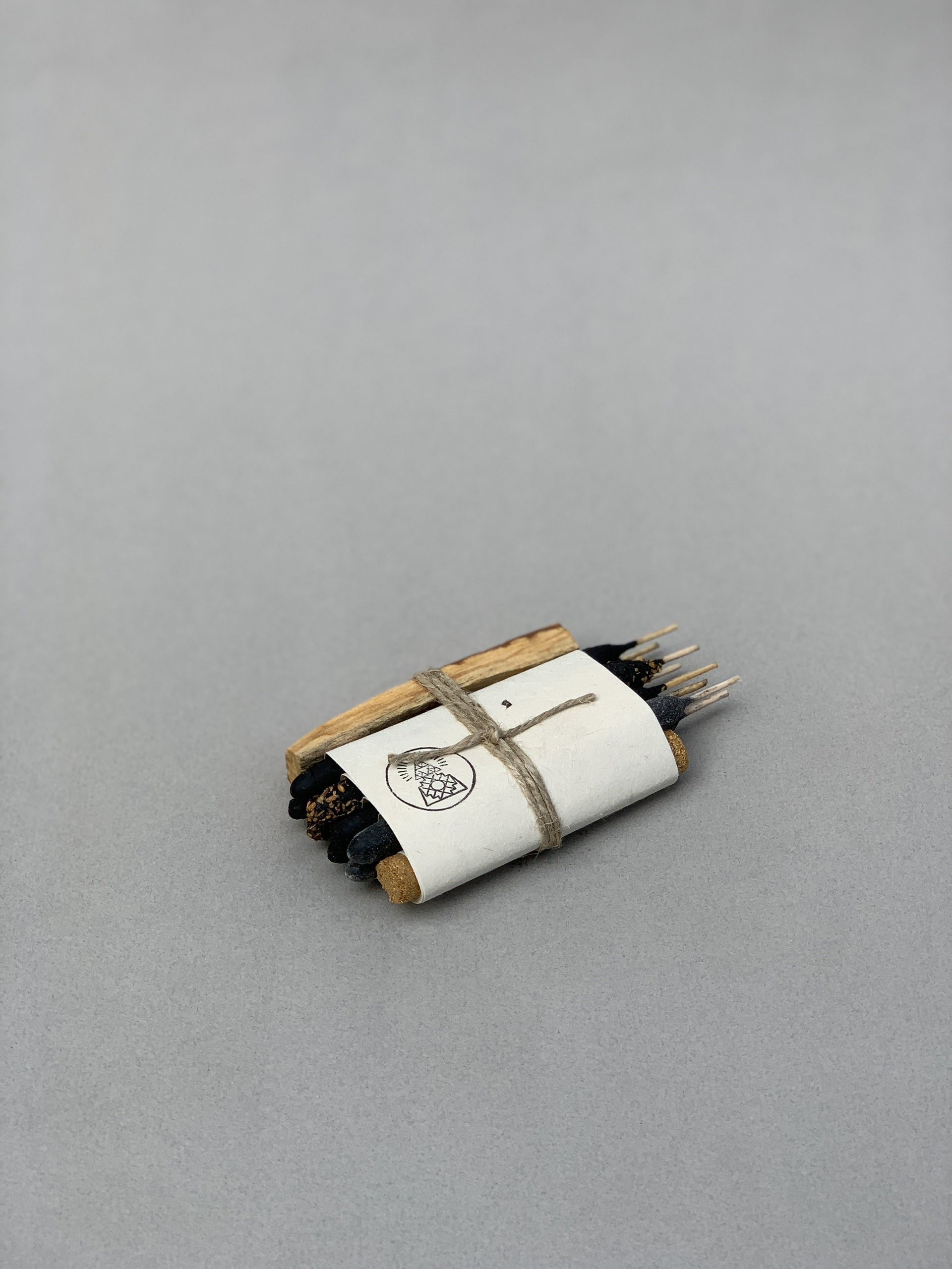 The Sampler Incense Bundle | Incausa features dark sticks, palo santo, and wood pieces wrapped in white paper and twine on a plain gray surface.