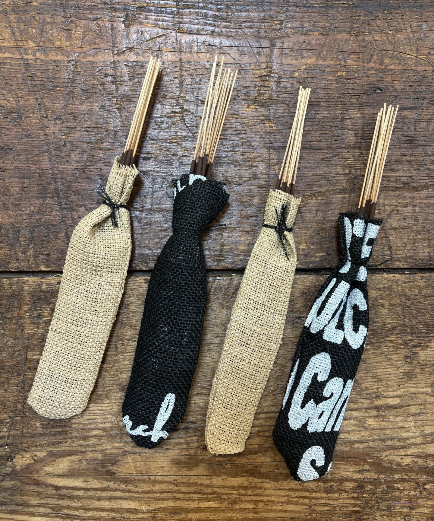 Four bundles of Incense Sticks | Glampfire by Ballad of the Bird Dog—two plain and two with black and white patterns, wrapped in upcycled coffee bags—rest on wood, adding a refined aroma to your space.