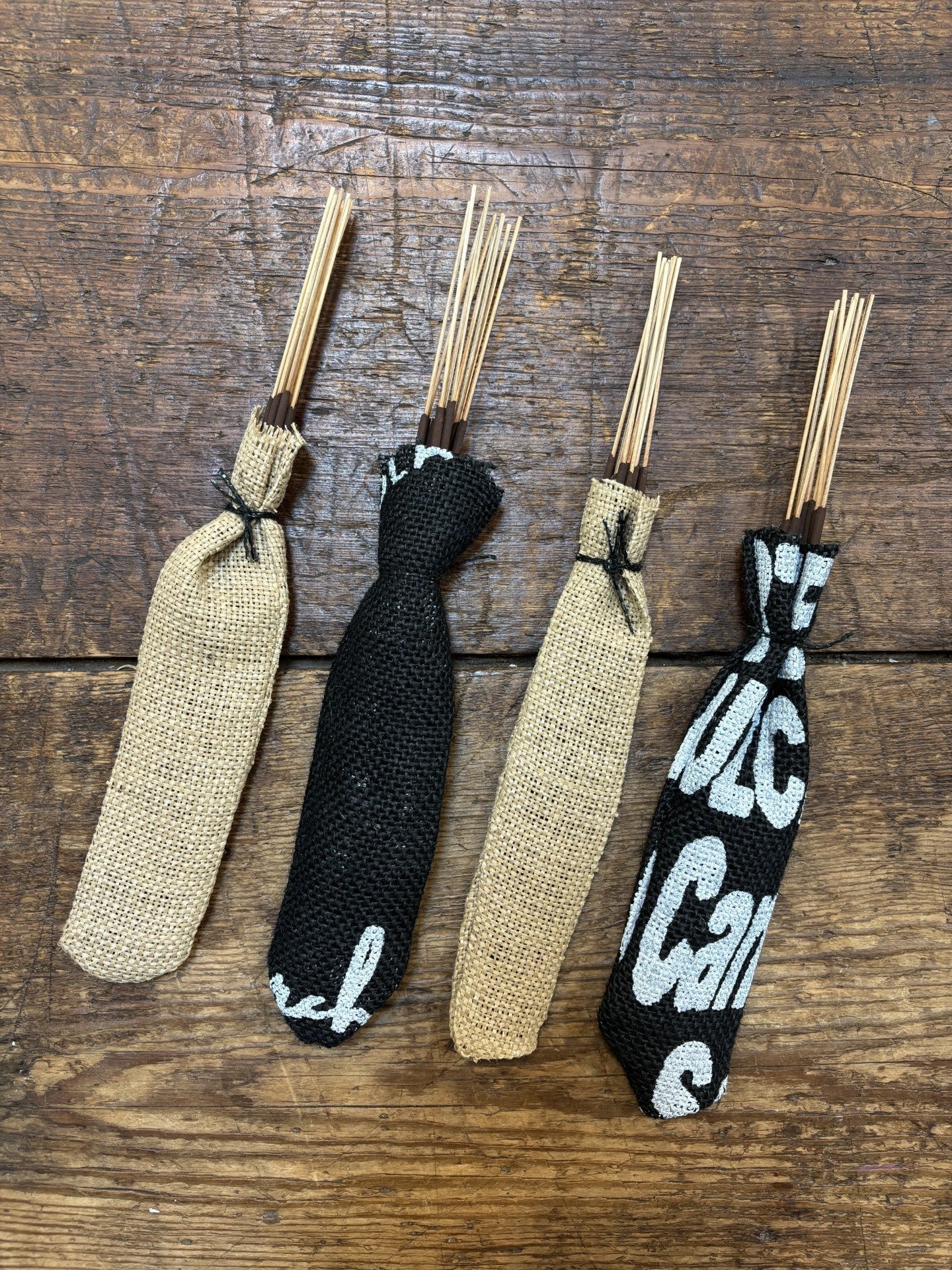 Four bundles of Ballad of the Bird Dog Incense Sticks | Tattoo Ink, wrapped in burlap and upcycled coffee bags, are arranged side by side on a wooden surface.