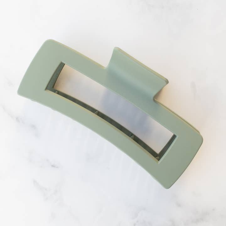 The Jumbo Square Hair Clip by Tiepology is a large, rectangular light green clip with a cut-out center, shown on a white marble surface.