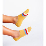 Wearing Kelly No Show Sock by Tailored Union—yellow lightweight socks with red, white, and blue stripes—the person lifts their feet against a plain white background.