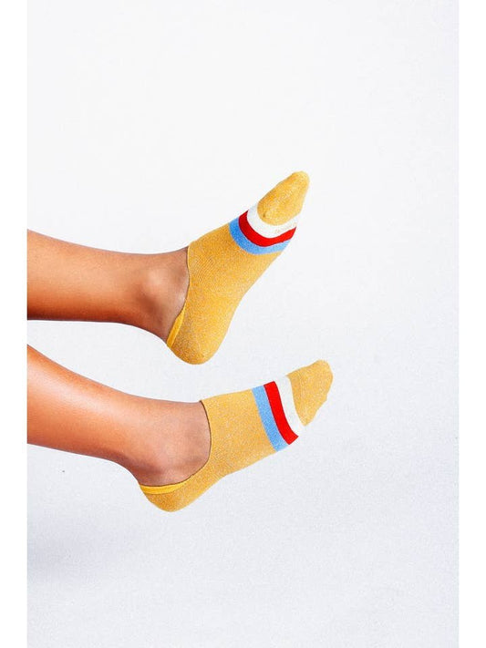 Wearing Kelly No Show Sock by Tailored Union—yellow lightweight socks with red, white, and blue stripes—the person lifts their feet against a plain white background.