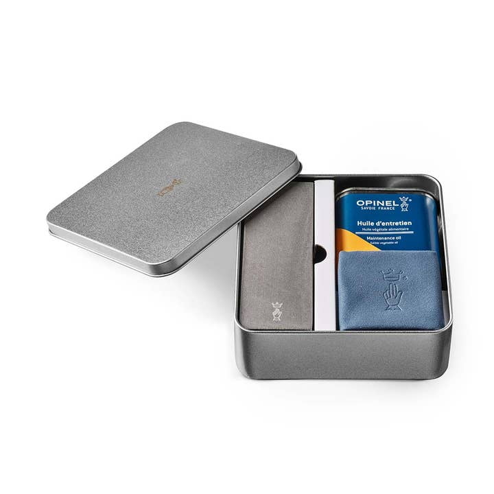 The Opinel Knife Maintenance Kit comes in a metal tin with the lid partially open, containing plant-based oil, a blue cloth, gray sharpening stone, and an instruction booklet.