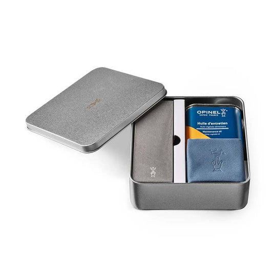 The Opinel Knife Maintenance Kit comes in a metal box and includes a sharpening stone, plant-based oil can, blue cloth, and a rectangular accessory—all neatly organized.