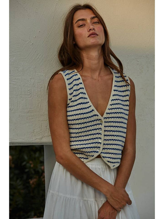 Woman wears the By Together Knit Sweater Cotton Striped Buttondown V-Neck Vest in cream and blue over a white dress, standing against a textured white wall.