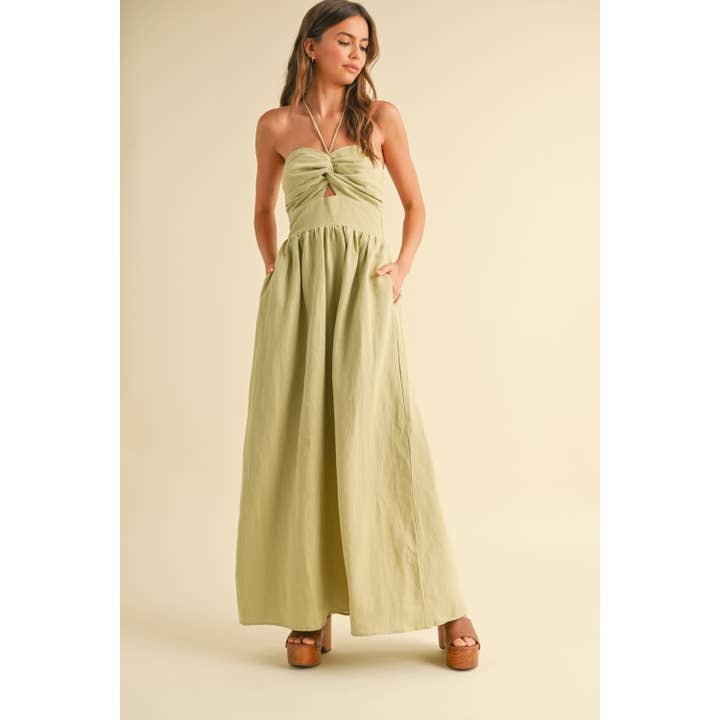 A woman in size S wears the Knotted Front Halter Neck Dress by Miou Muse—a light green, linen-cotton dress with a gathered bust—standing against a beige background.