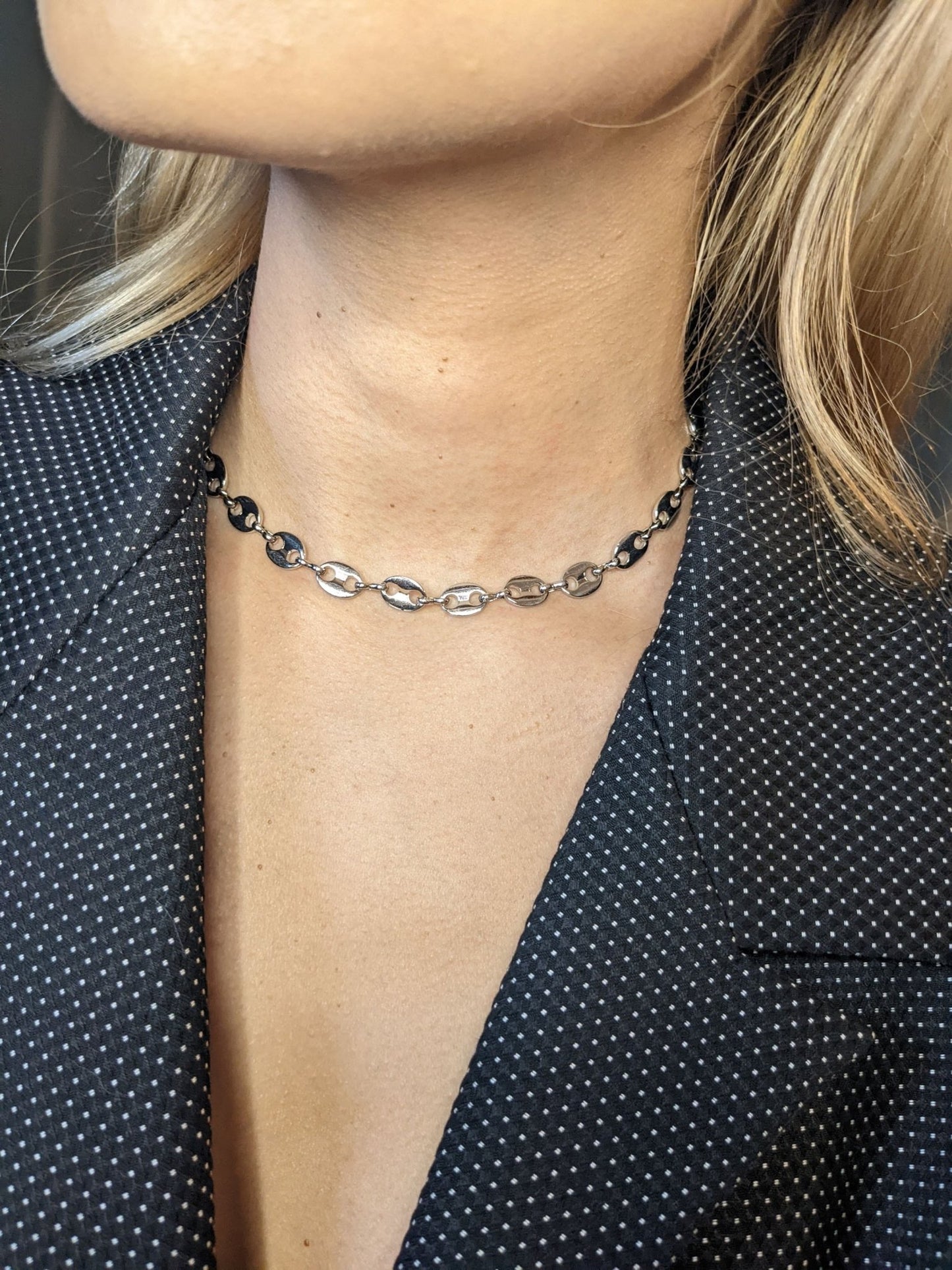 A person wears the Koffee Necklace by Minh Atelier, a silver and black choker that shines elegantly against a dark, polka-dotted blazer.