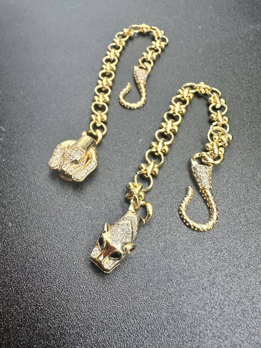 The La Prise Bracelet by Minh Atelier features two 18k gold-plated chain bracelets with panther and elephant head clasps, each set with sparkling clear stones, elegantly displayed on a black surface.