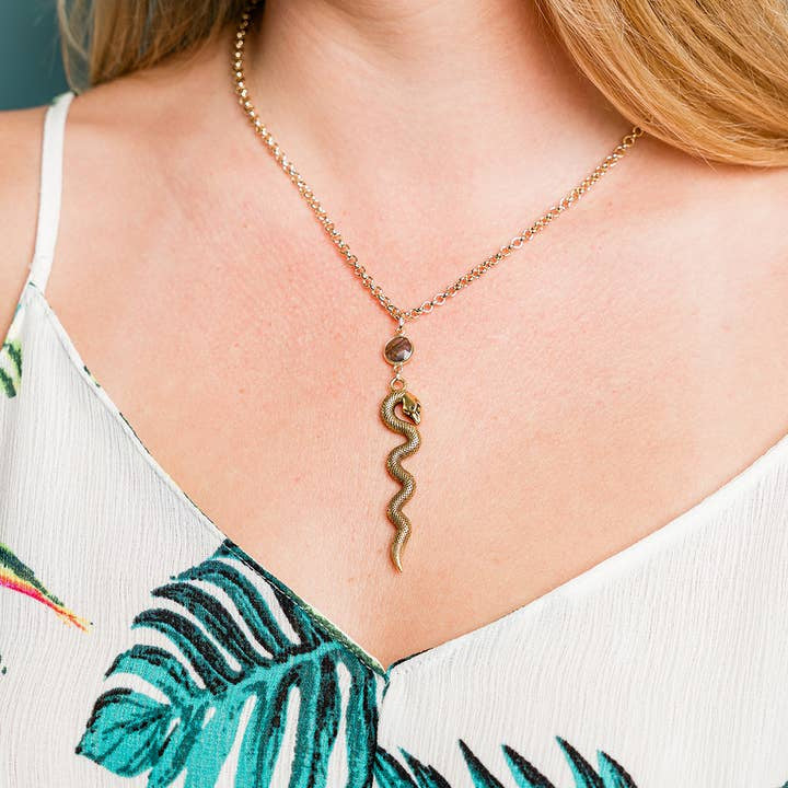 A person wearing the Labradorite Serpent Necklace by Ornamental Things with a rolo chain, paired with a white, leaf-patterned top.
