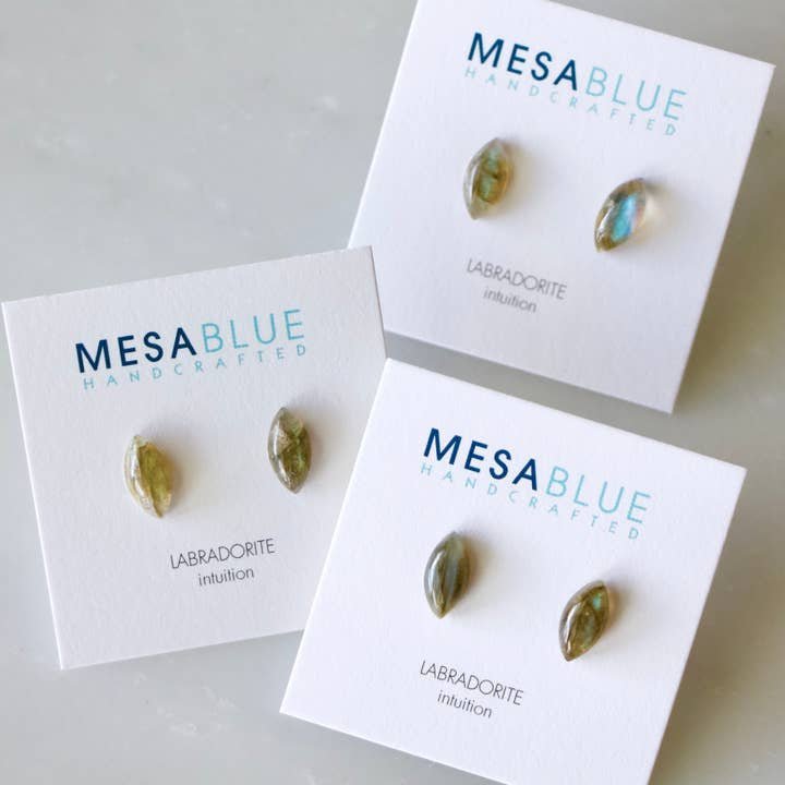 Three pairs of Labradorite Stud Earrings from Mesa Blue are shown on cards labeled "MESA BLUE HANDCRAFTED LABRADORITE intuition," each featuring stainless steel ear posts for comfort.