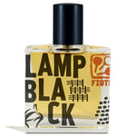 A clear glass perfume bottle with black cap holds amber liquid. The label shows "Lampblack | Fzotic" in bold black letters with red graphics, evoking oud and woody-smoky scents in this Fzotic fragrance.