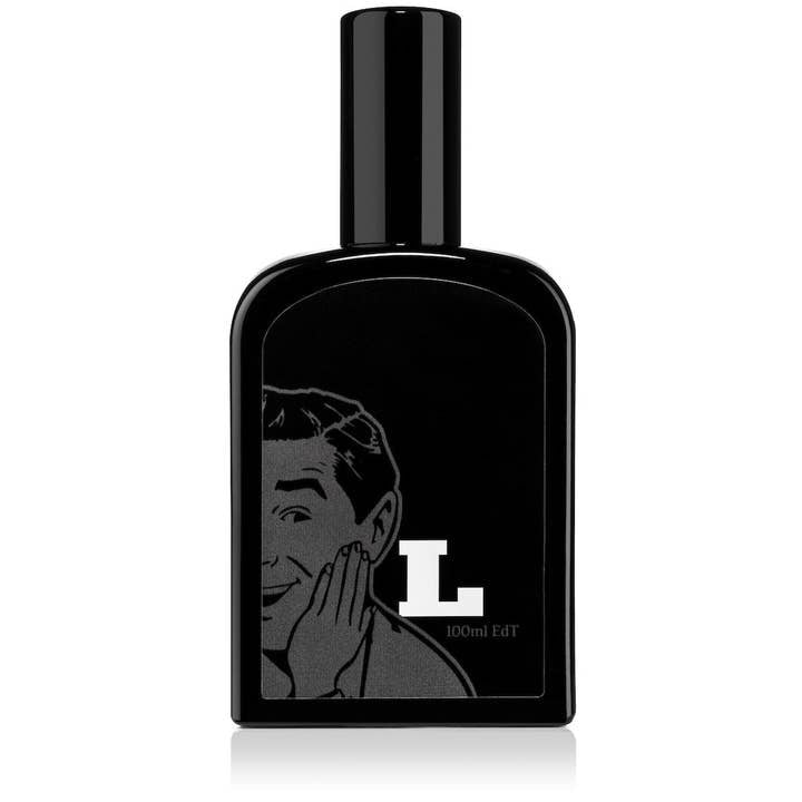 The Latigo Eau De Toilette by Fine Accoutrements comes in a 100 ml black glass bottle with a smiling man and large white "L" graphic. It features a diffusive atomizer cap for easy application.