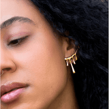 Close-up of a person with curly dark hair wearing the Lava Studs by Peter and June, 18k gold plated earrings with a dripping design, along with a small nose ring.