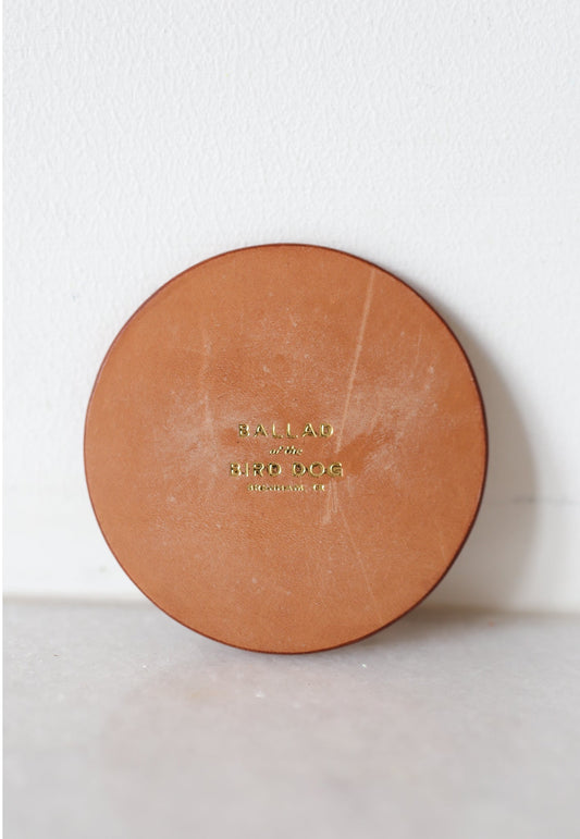 A handmade round leather coaster by Ballad of the Bird Dog, embossed with "BALLAD with HIRO OGG," shown against a white background. Product: Leather Coaster | Round | Ballad of the Bird Dog.