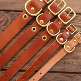 Five handmade brown “Leather Dog Collar | Ballad of the Bird Dog” by Ballad of the Bird Dog, featuring gold buckles and grommets, are displayed side by side on a rustic wooden surface in classic English bridle style.