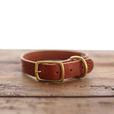 The Leather Dog Collar by Ballad of the Bird Dog is a handmade English bridle collar in brown leather with a brass buckle and D-ring, crafted in Brenham and displayed on a wooden surface.