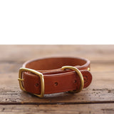 The Leather Dog Collar by Ballad of the Bird Dog, crafted from brown English bridle leather with a gold-colored buckle and D-ring, is displayed on a wooden surface.