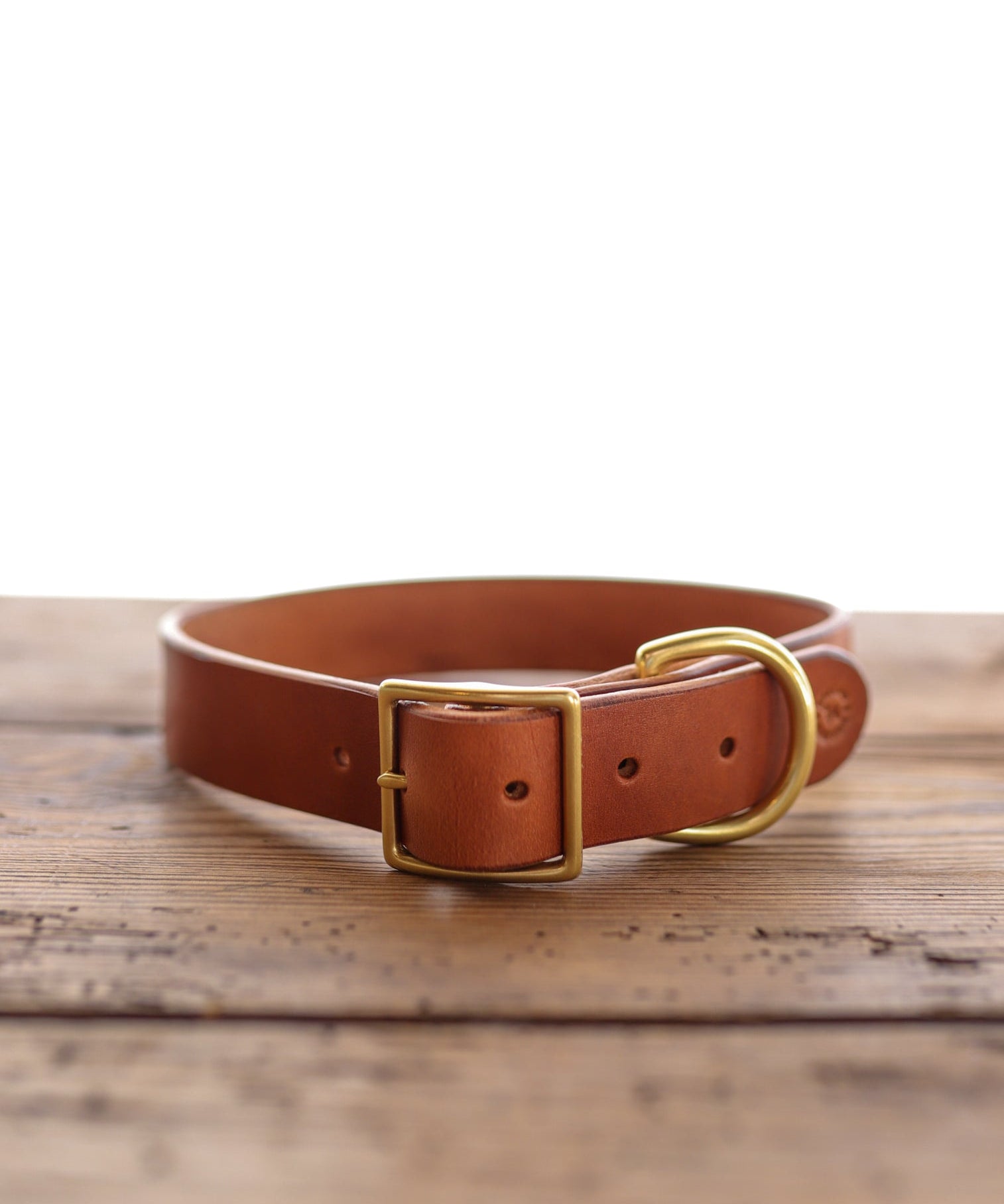 The Leather Dog Collar by Ballad of the Bird Dog features handmade brown leather, a brass buckle, and D-ring, shown on wood with a white background. Crafted in Brenham for timeless quality and style—perfect for your dog.