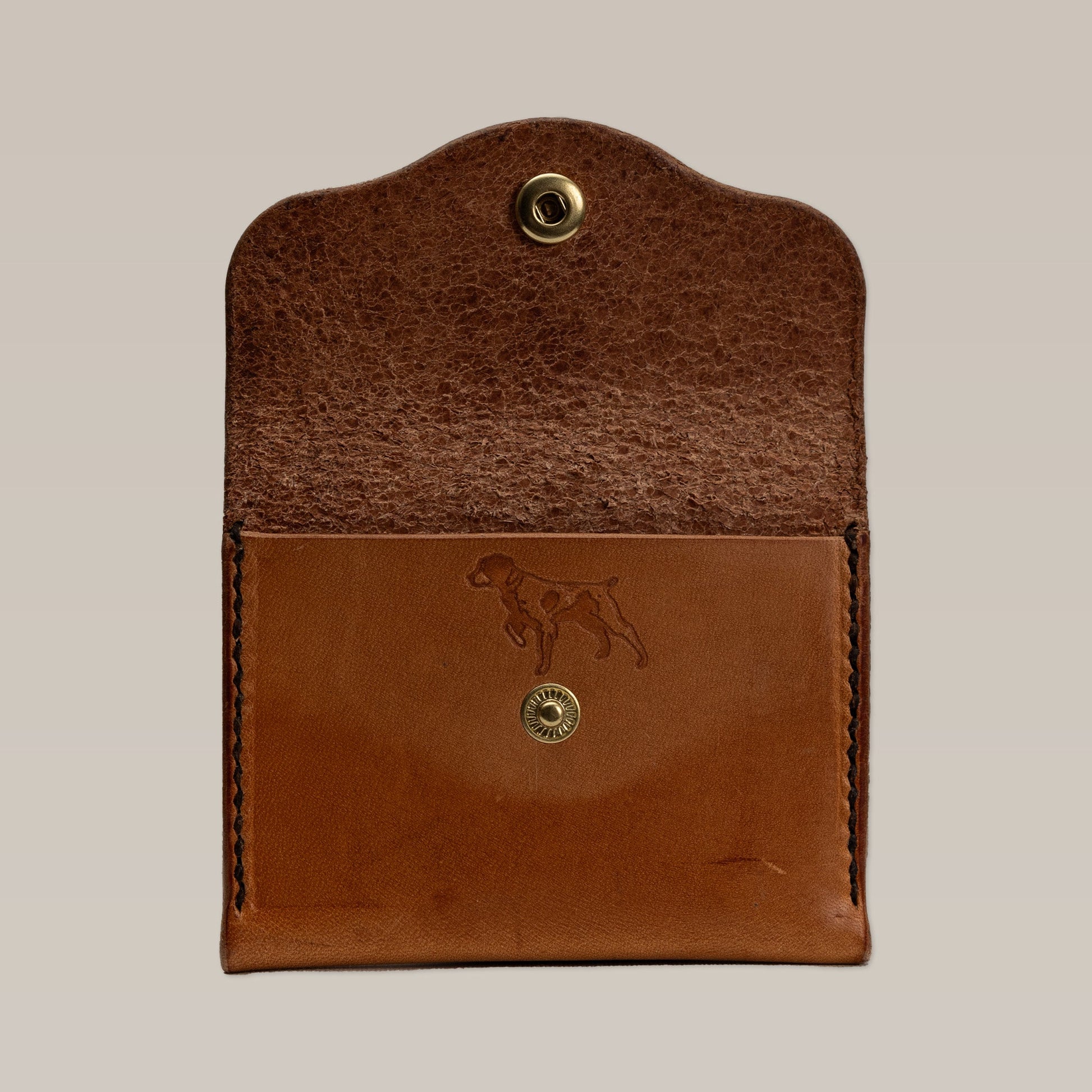 The Ballad of the Bird Dog Leather Wallet is a small card wallet in brown leather with a snap closure. Its front flap features an embossed dog outline and it opens to reveal the interior.