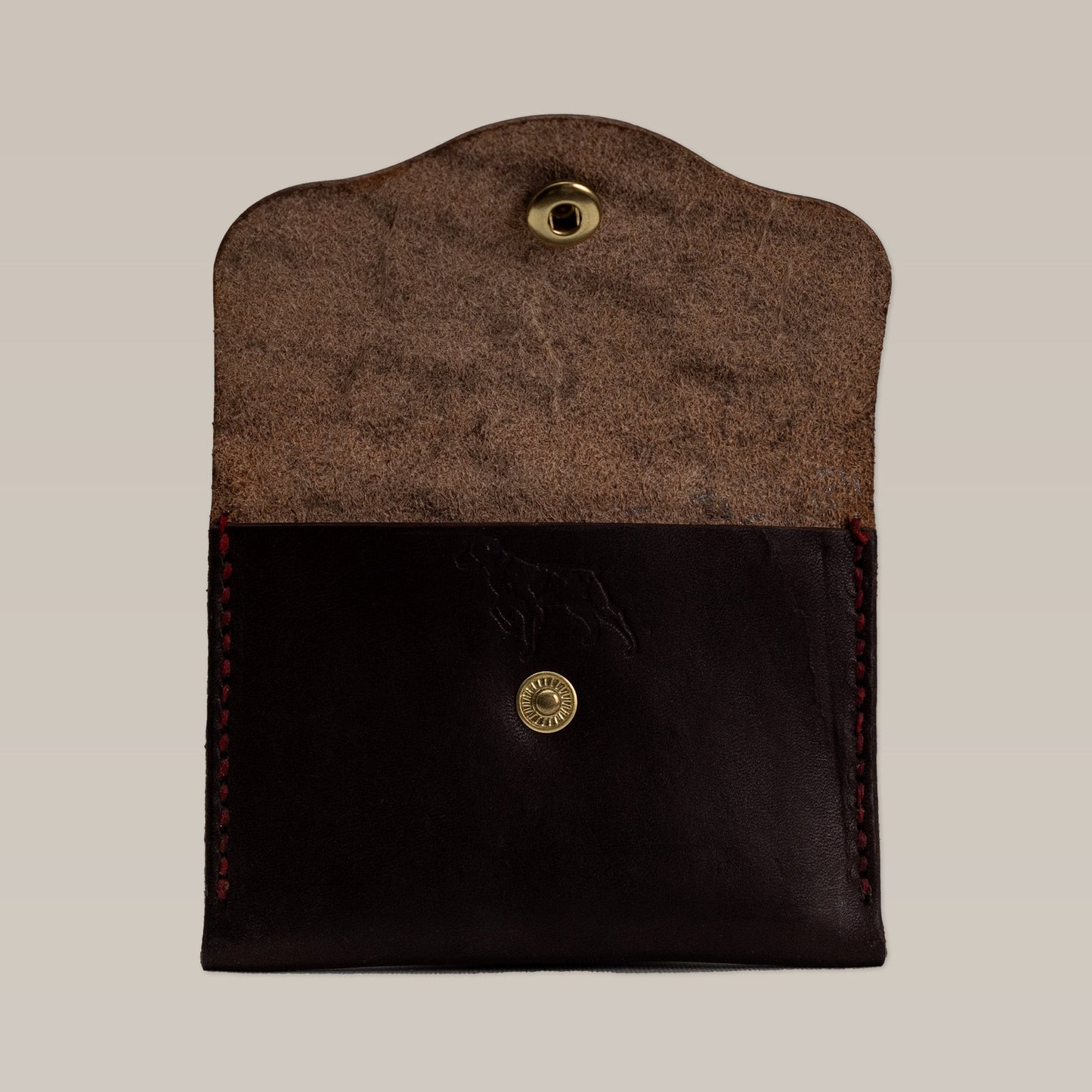 The Leather Wallet by Ballad of the Bird Dog features dark leather with red stitching, a suede interior, and a gold snap button closure—shown open on a neutral background.