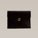 The Ballad of the Bird Dog Handcrafted Leather Wallet - Small Card Holder features dark brown leather with a brass snap button, artisanal quality, and is photographed on a plain light beige background.