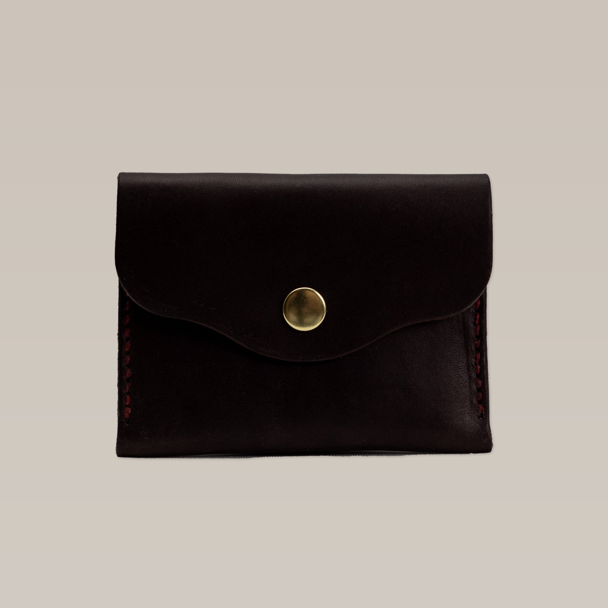 The Ballad of the Bird Dog Handcrafted Leather Wallet is a small, dark brown card holder with red stitching and a brass snap button, highlighting artisanal quality against a plain light background.