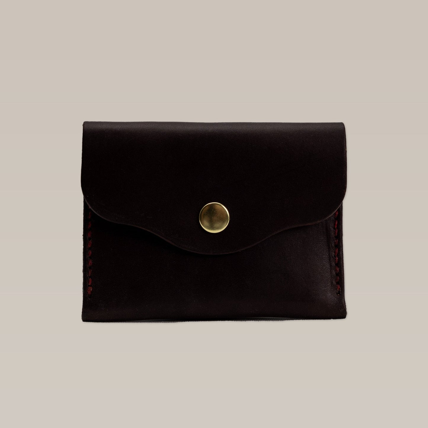 A closed dark brown Leather Wallet by Ballad of the Bird Dog, featuring a brass snap button, is shown against a plain light background.