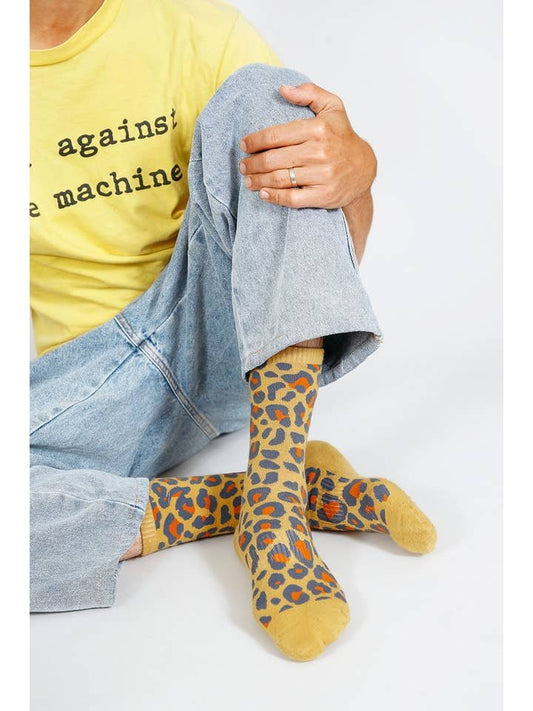 A person wearing light blue jeans, a yellow graphic t-shirt, and Tailored Union's Leo Crew Sock sits cross-legged on the floor.
