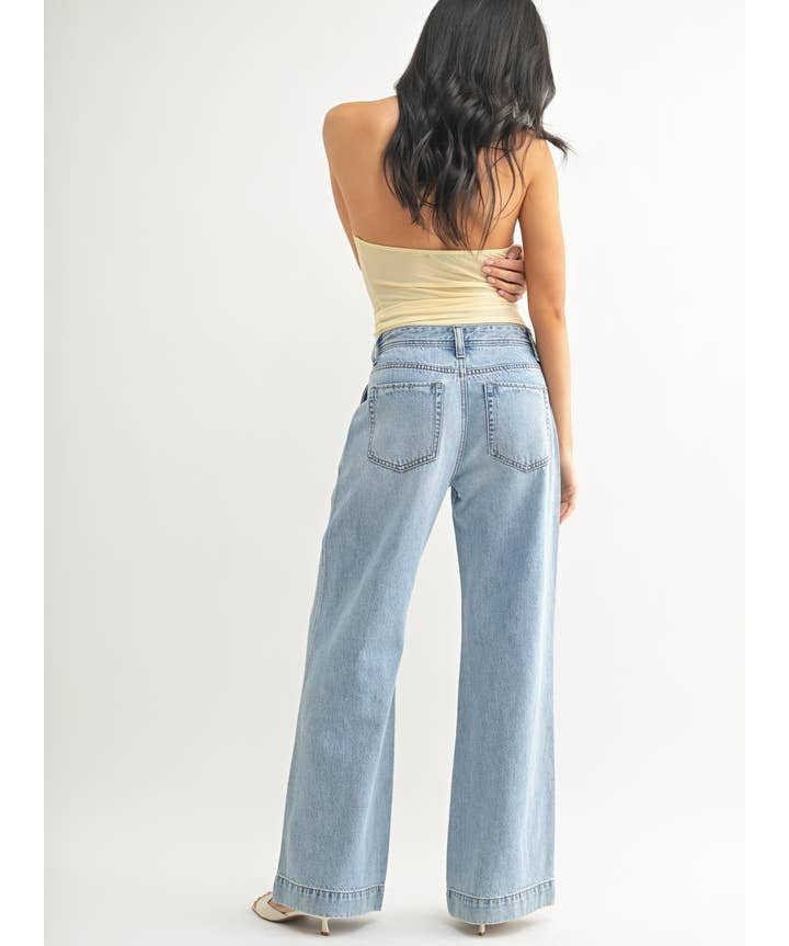 A woman faces away, wearing a strapless beige top and JBD's Lightweight Drapey Relaxed Trouser—high-waisted, wide-leg jeans in light denim—against a plain white background.