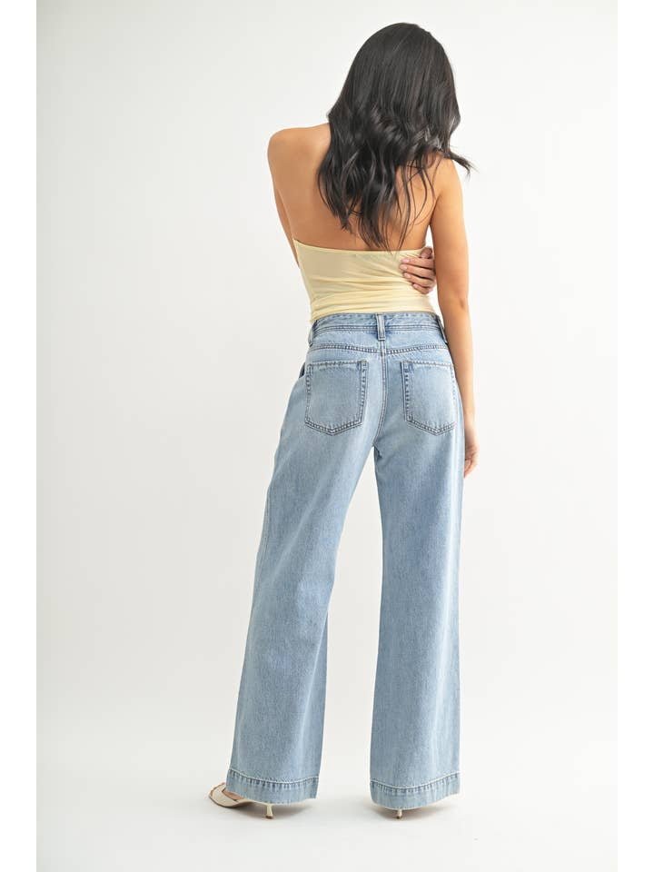 A woman stands with her back to the camera, wearing the JBD Lightweight Drapey Relaxed Trouser, wide-leg light denim jeans, paired with a strapless beige top against a plain white background.