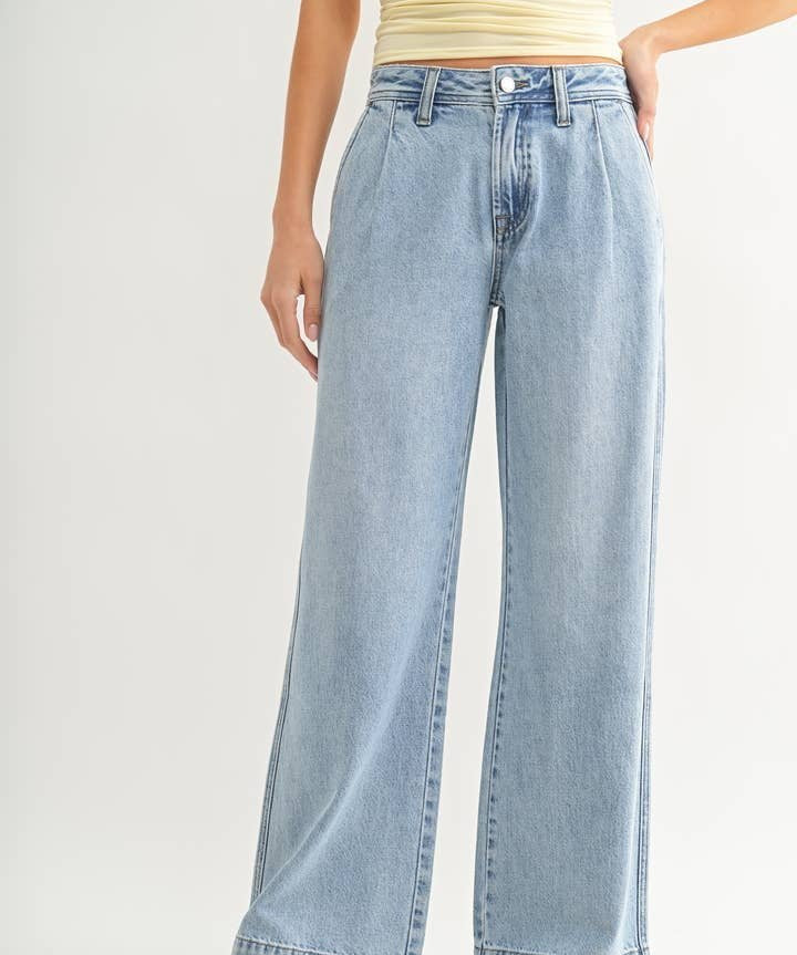 A person wearing JBD's Lightweight Drapey Relaxed Trouser, a high-waisted, light denim wide-leg jean, paired with a pale yellow sleeveless top, stands against a plain background.