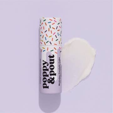 A Poppy & Pout Lip Balm tube with a sprinkle-decorated cap sits beside a white cream smear on a light purple background, showcasing this natural, cruelty-free balm.