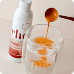 A spoon pours orange liquid into water beside a bottle labeled "Liposomal Curcumin + Resveratrol | Rho Nutrition," featuring turmeric root extract from Rho Nutrition.
