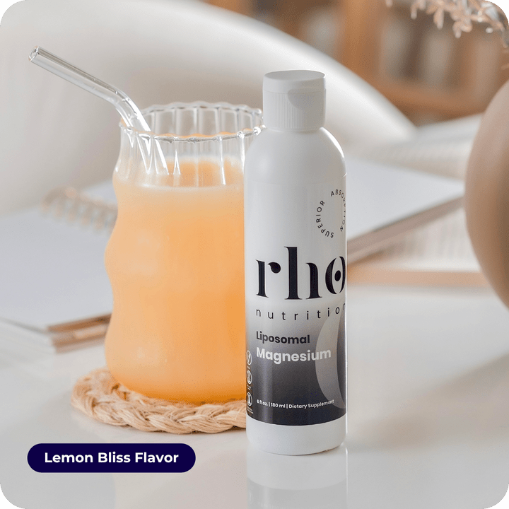 A bottle of Liposomal Magnesium | Rho Nutrition sits by a glass of orange drink with a glass straw on a white table. The "Lemon Bliss Flavor" label highlights magnesium for muscle recovery and nervous system support.