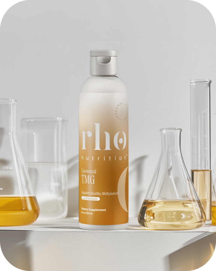 A bottle of Liposomal TMG by Rho Nutrition sits on a white surface, with three glass beakers filled with yellow liquids in the background, highlighting support for healthy homocysteine metabolism.