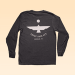 The Ballad of the Bird Dog Shop Shirt Long Sleeve | Thunderbird is a black tee with a bold geometric eagle, "TRUST YOUR GUT," and "Brenham, TX" on the back, set against a beige backdrop.