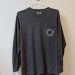 The Ballad of the Bird Dog Shop Shirt Long Sleeve | Thunderbird is a dark gray tee with a chest pocket, featuring a circular white graphic and text, displayed on a hanger against a plain wall.