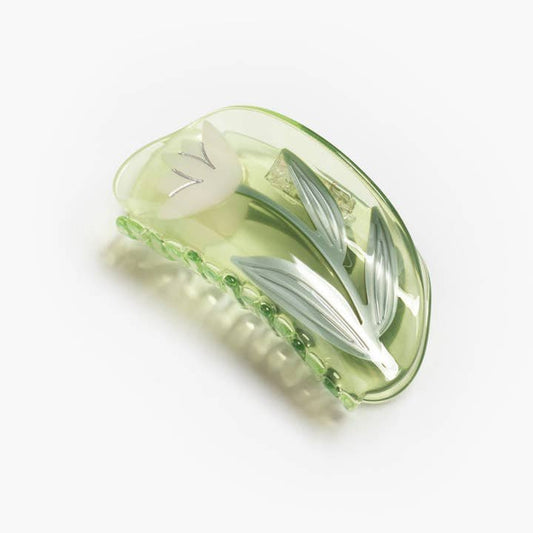 The Winona Irene Lotus Flower Hair Claw in clear green acetate features a delicate white tulip with green leaves, inspired by the vibrant paddle boats at Echo Park’s Lotus Festival.