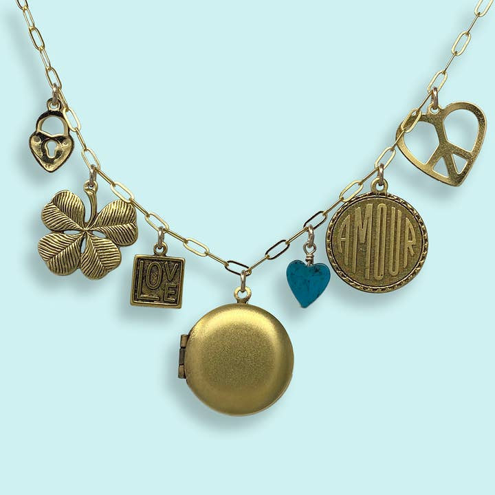 The Love and Luck Charm Necklace by Ornamental Things is a gold cable chain necklace featuring seven unique charms, displayed on a light blue background.