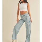 A woman poses against a plain light background, wearing a white sleeveless crop top, beige sneakers, and JBD's Lt - Cargo Jean—light blue high-rise cargo jeans.
