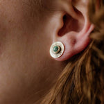 Close-up of a person's ear wearing Madison Studs by CommonForm, featuring a round brass disc with a turquoise stone at the center.