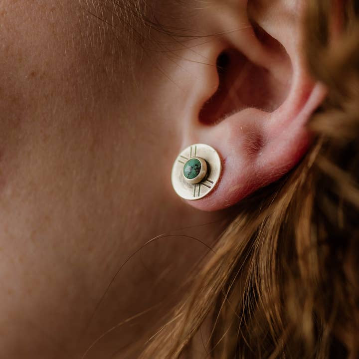 Close-up of a person's ear wearing Madison Studs by CommonForm—sterling silver earrings featuring a green center stone and engraved radiating lines.
